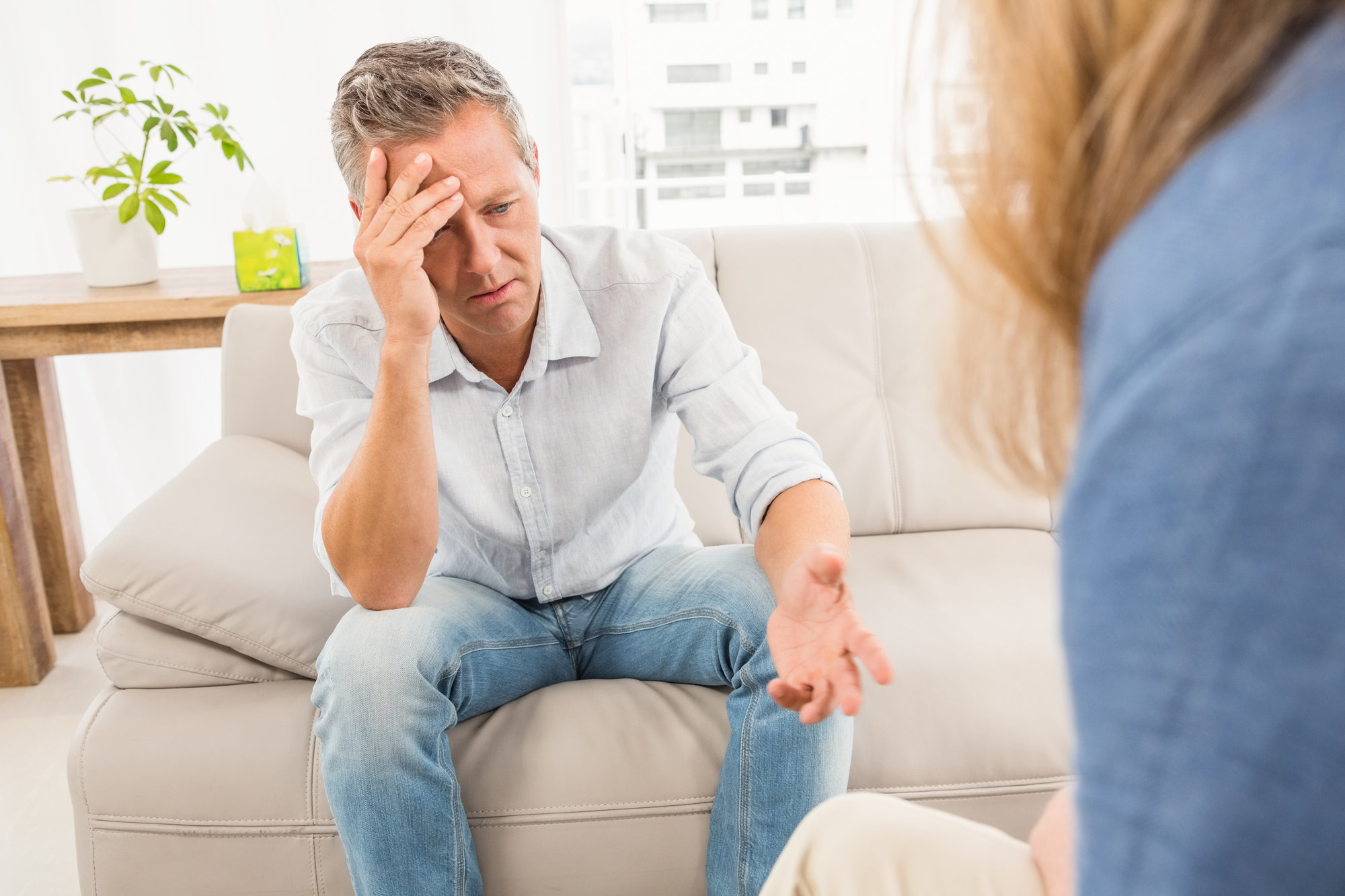 Worried man sitting on couch and talking to therapist in the office